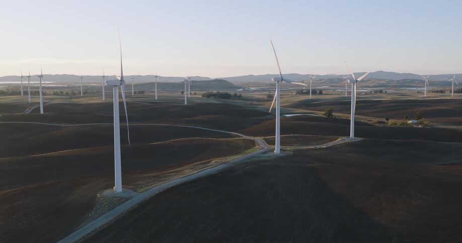 Wind turbines spin on a wind farm with mountains in the distance