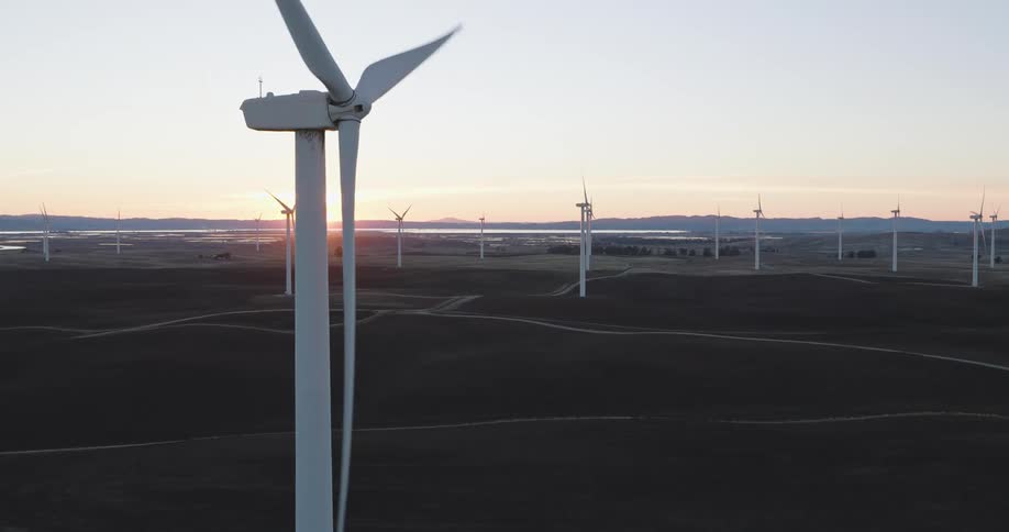 Panorama of wind turbine engines in motion with the sunrise on the horizon