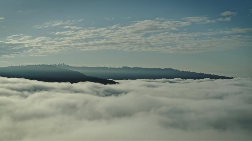 Mountains protrude above a thick layer of clouds during the daytime