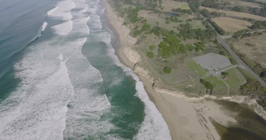 Aerial of ocean waves rolling into a sandy beach during the daytime