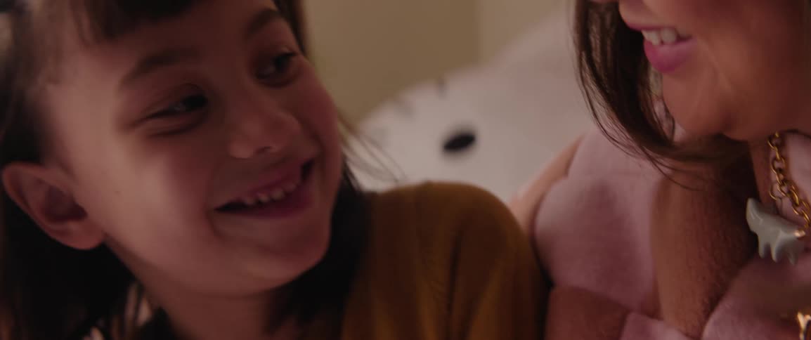 A young girl sits next to her mother while they talk and smile at each other