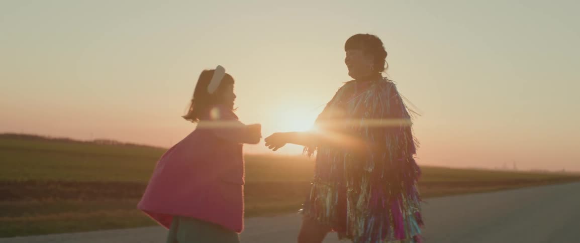 A woman and a young girl dancing in the middle of a rural road at sunset