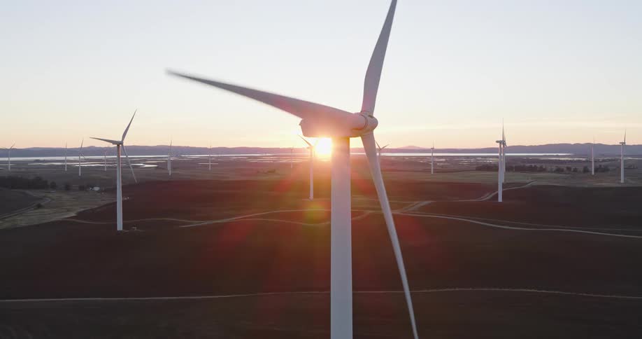 Wind turbine arms spinning on top of a windmill on a wind farm at sunset