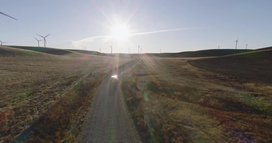 A van travels on a rural road through a wind farm