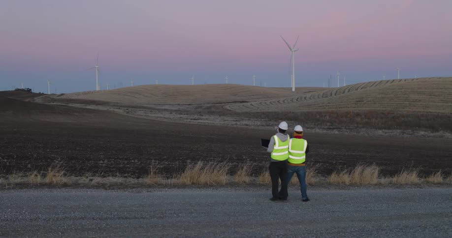 Two workers analyzing a field with wind energy platforms on a day with a purple sky