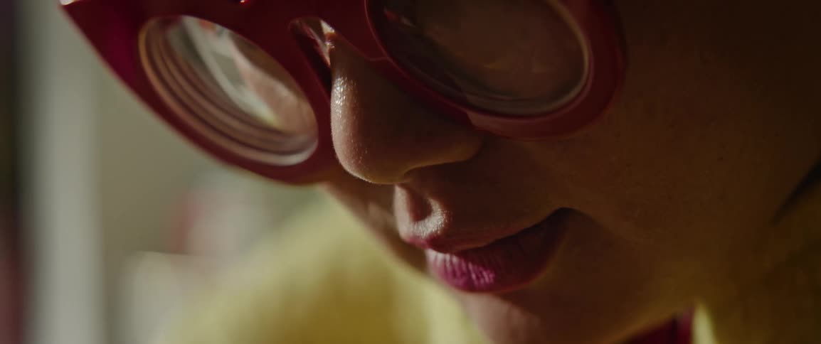 A woman is wearing large red glasses while working in extreme close up