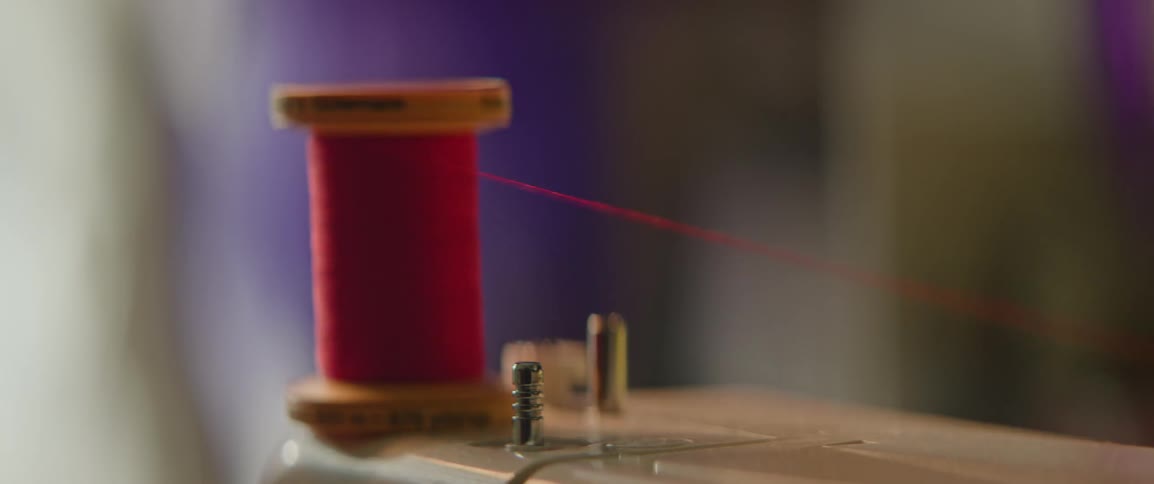 Closeup of a roll of red thread feeding into a sewing machine