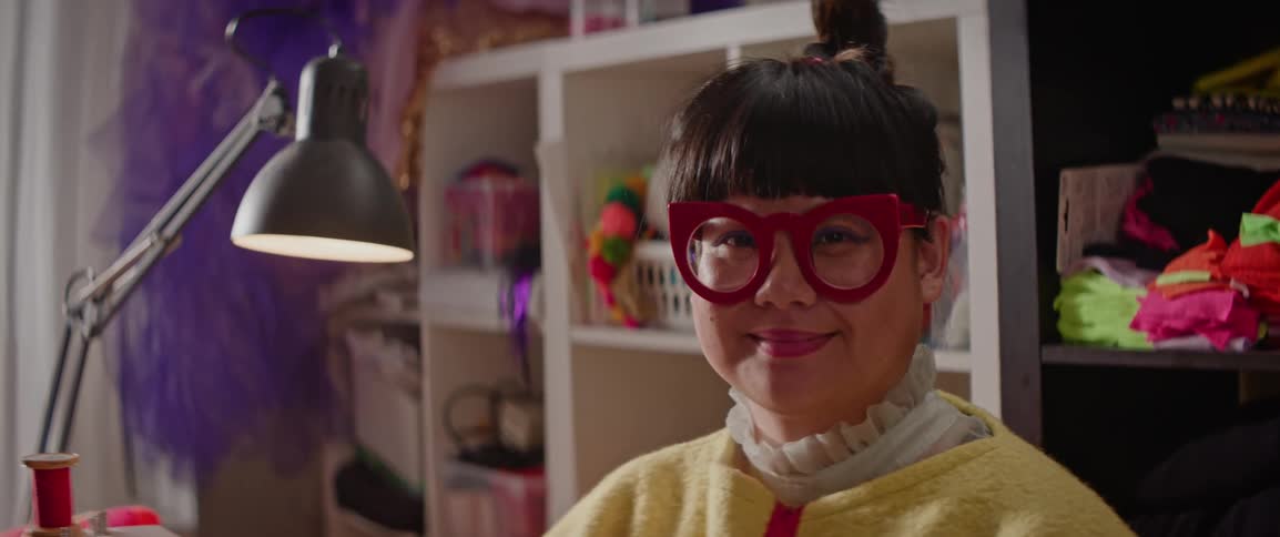 Portrait of a woman with large red glasses in her sewing room