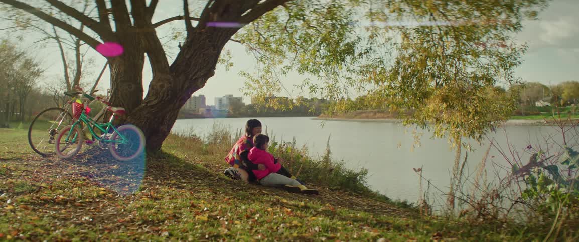 A mother talks to her daughter while sitting on a river bank on an autumn day