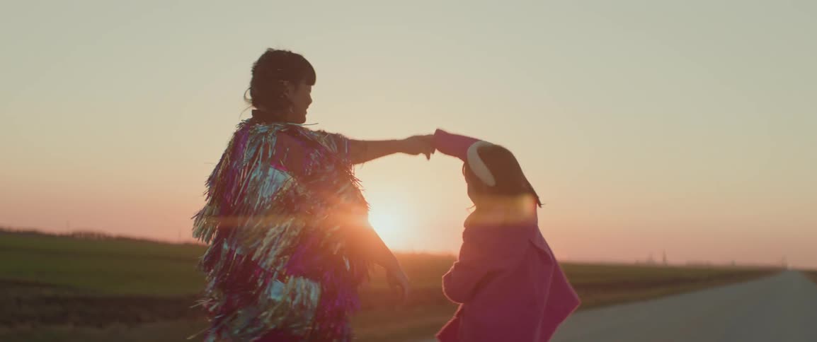 Woman dances with her daughter on a road between fields as the sun sets