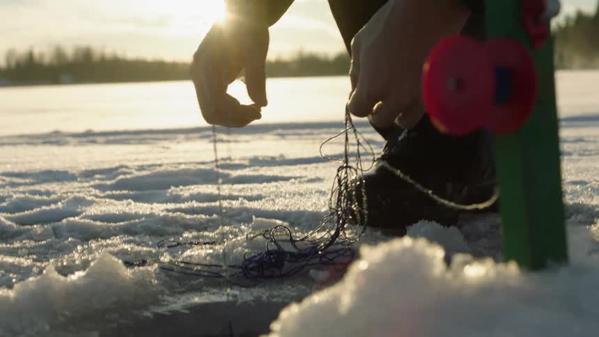 A man pulls tangled fishing line from a hole in a frozen lake