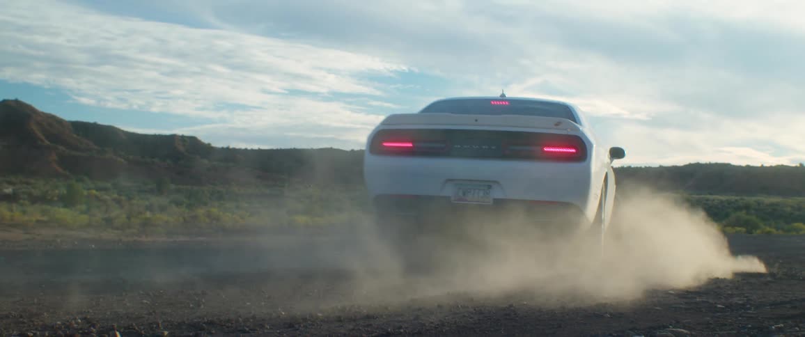 White sports car kicks dust driving over gravel