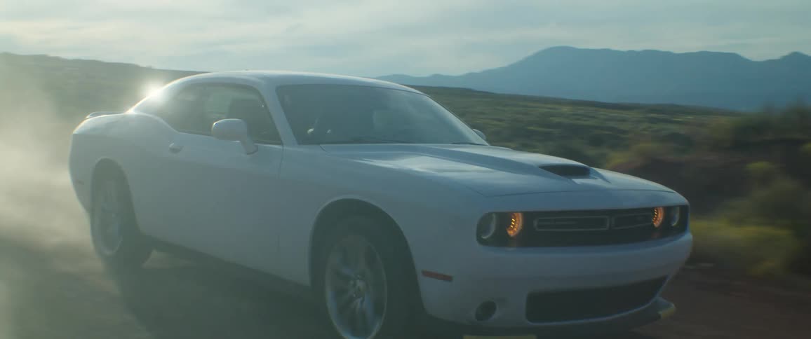 A white car driving on a dirt road as dust flies around