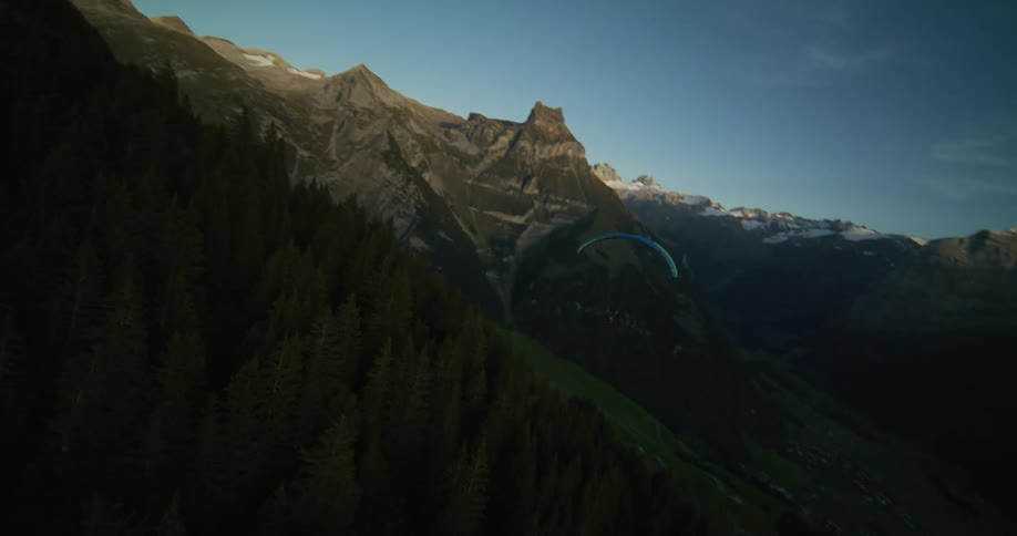 A man flying a paraglider floats along the side of a mountain cliff