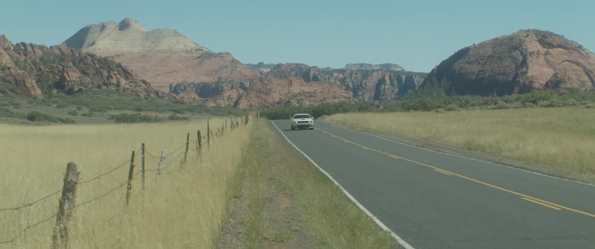 A white dodge car driving by a tarred road in the country side