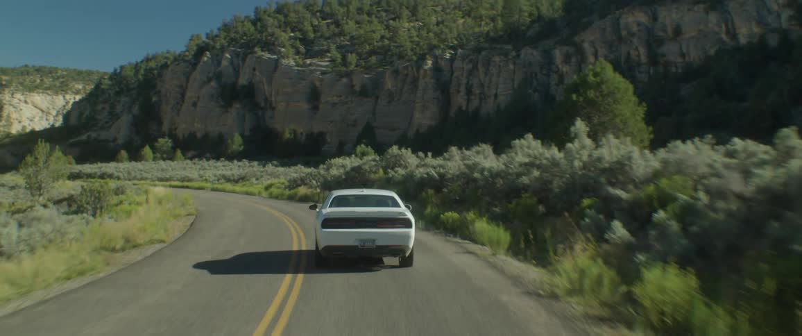 A white dodge car driving in a freeway on the countryside