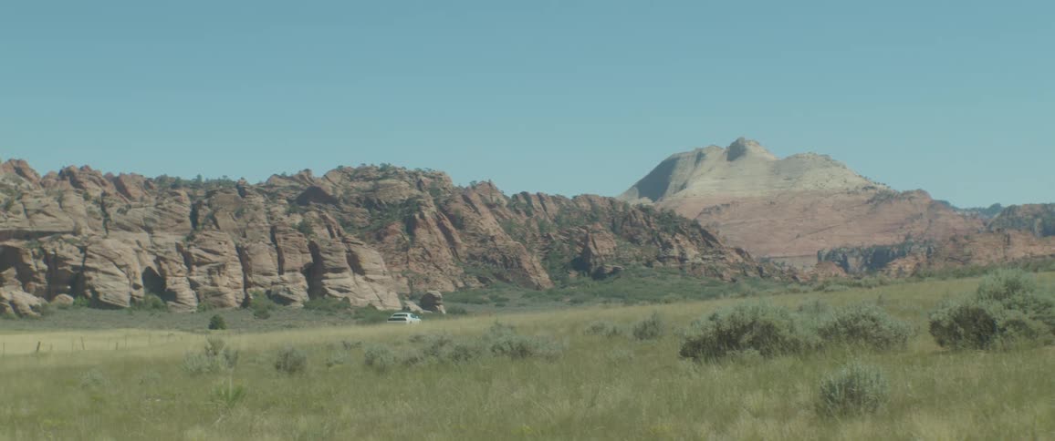 A white car driving on a rural road with vegetation and mountains around