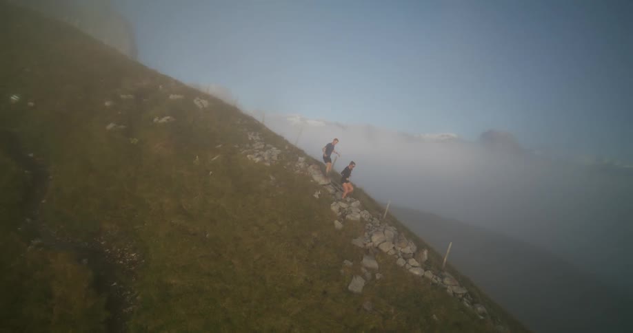 Aerial view of two people running on a mountain ridge under the clouds