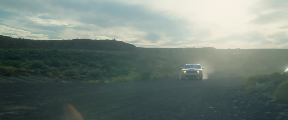 A white sports car driving on a dirt road and kicking up dust wherever it goes