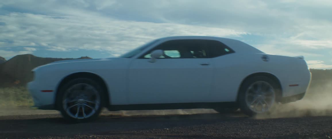 A white dodge car driving on a dirt road