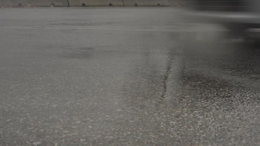 Several vehicles passing through a puddle of water on an asphalt road