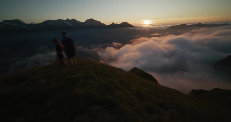 Aerial view of a couple standing on a mountain ridge at sunset