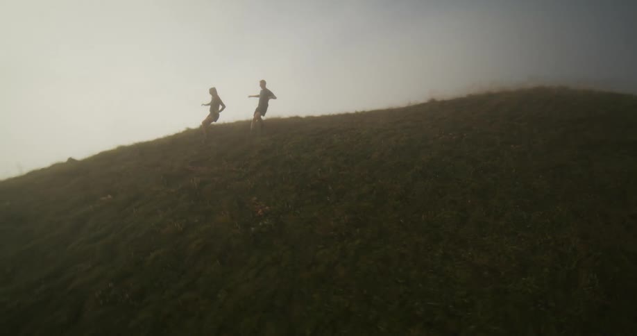 Two people are running down from the top of a hill and there is a big fog below them