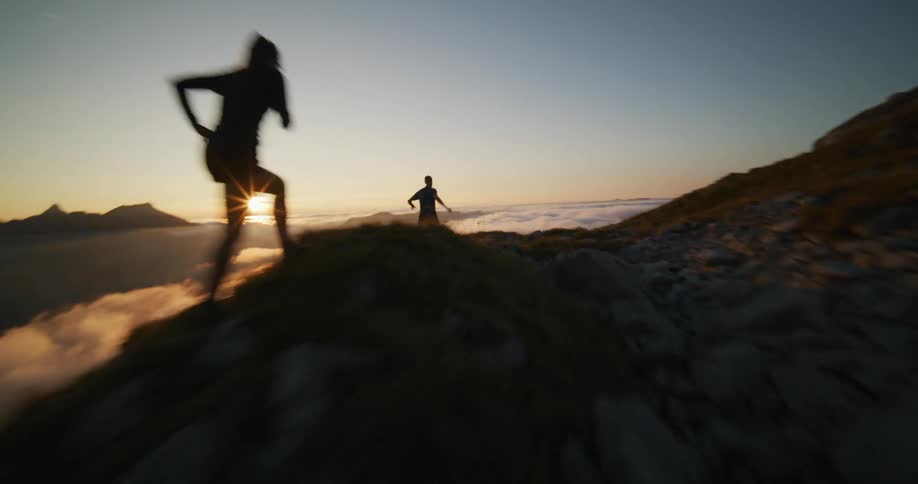Couple running over the ridge of a mountain at sunset