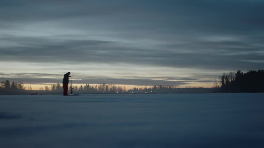 Man digs through the ice with a tool at sunset