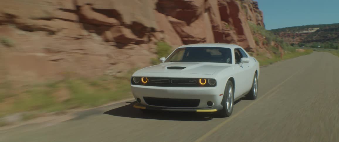 A white sports car travels on a road alongside a mountain