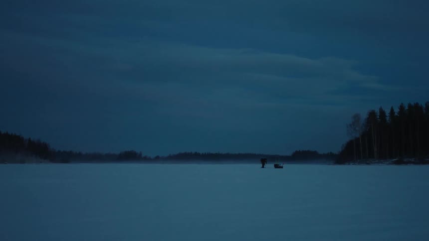 A person kneeling in the snow stands and walks over to a black shape
