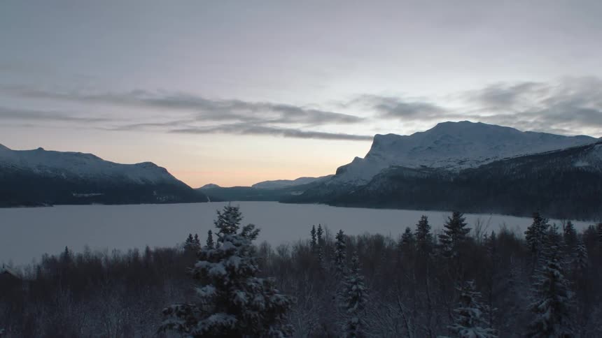 Sun rising over snowy mountains surrounding a body of water