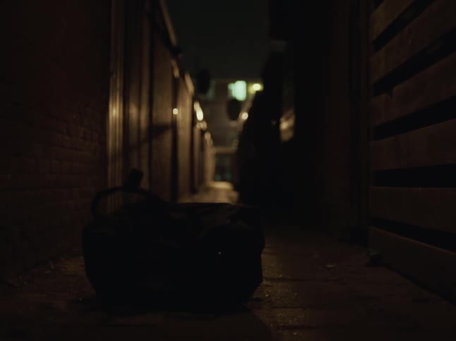 A man jumps down from atop a wall after throwing his backpack on the ground