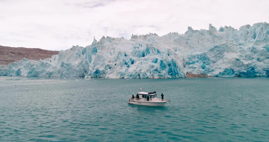 A boat with two people on it drives along a lake surrounded by snow covered mountains and vegetation
