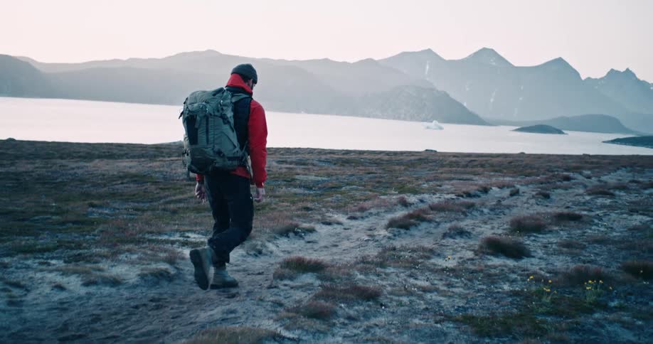 A hiker walking on a grassy frozen path near a lake