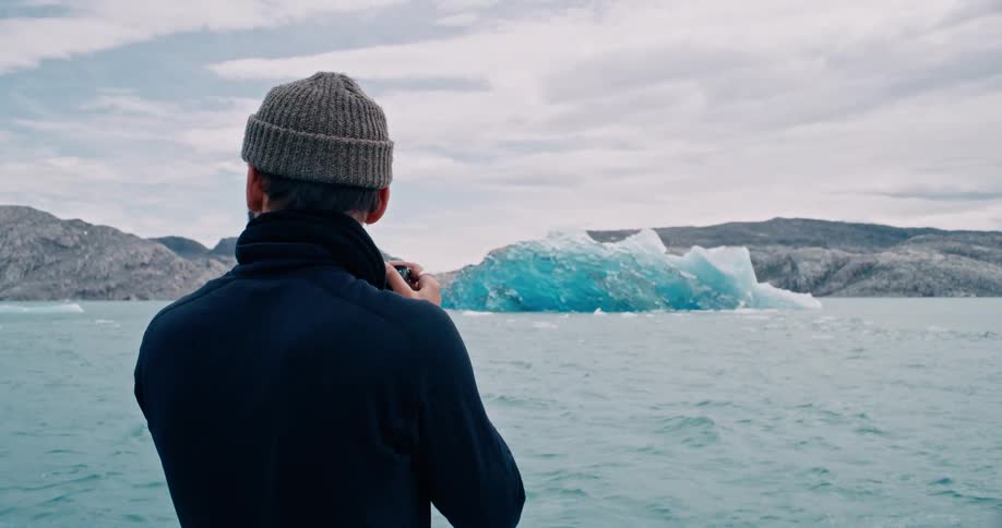 A man taking a photo of a melting iceberg
