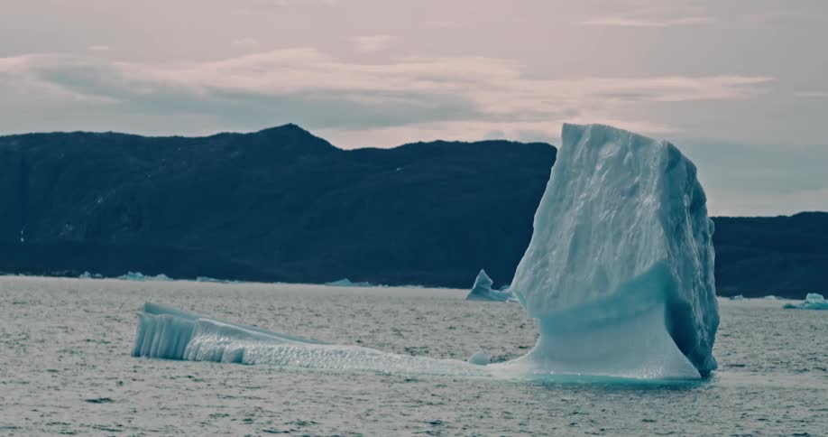 Melting iceberg floats off the arctic coast as birds fly in the distance