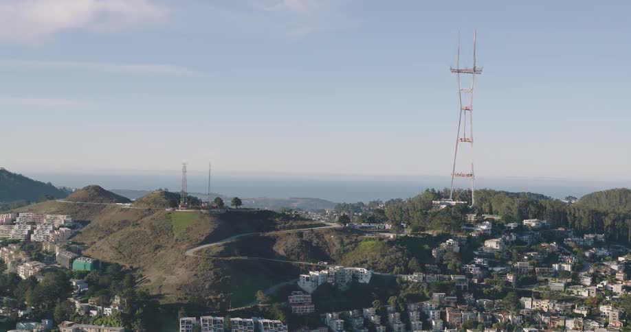Aerial panorama of houses and condominiums nestled in hills among mountains with an antenna tower on the peak on a day with a blue sky