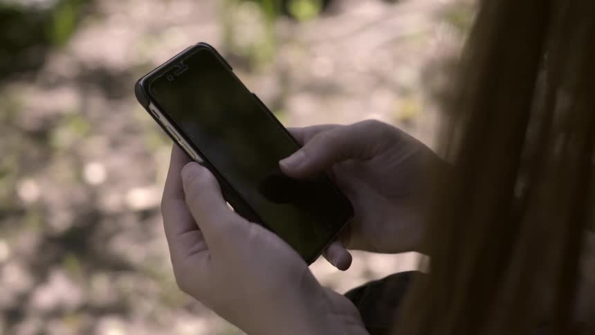 A woman browses on her phone outdoors