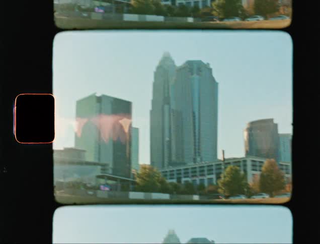 Vehicles drive past field toward downtown skyscrapers