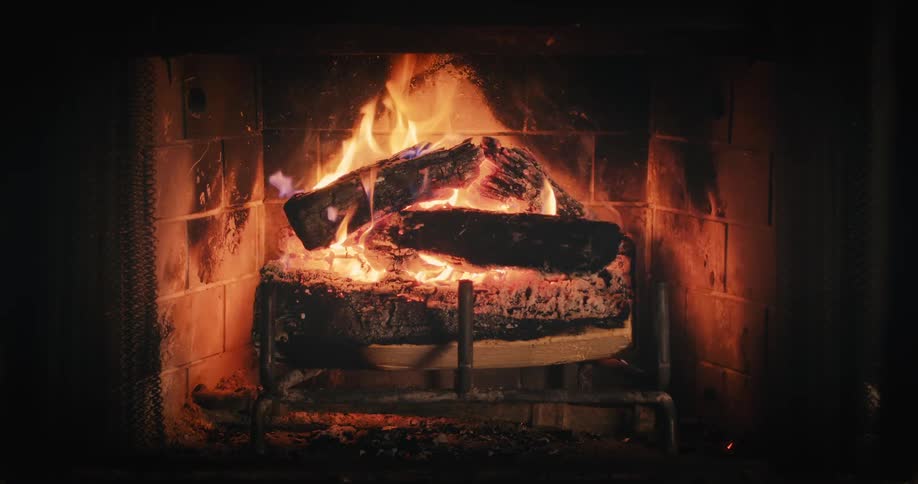 Flames flicker as wood burns in a fireplace as sparks fly when a log falls out