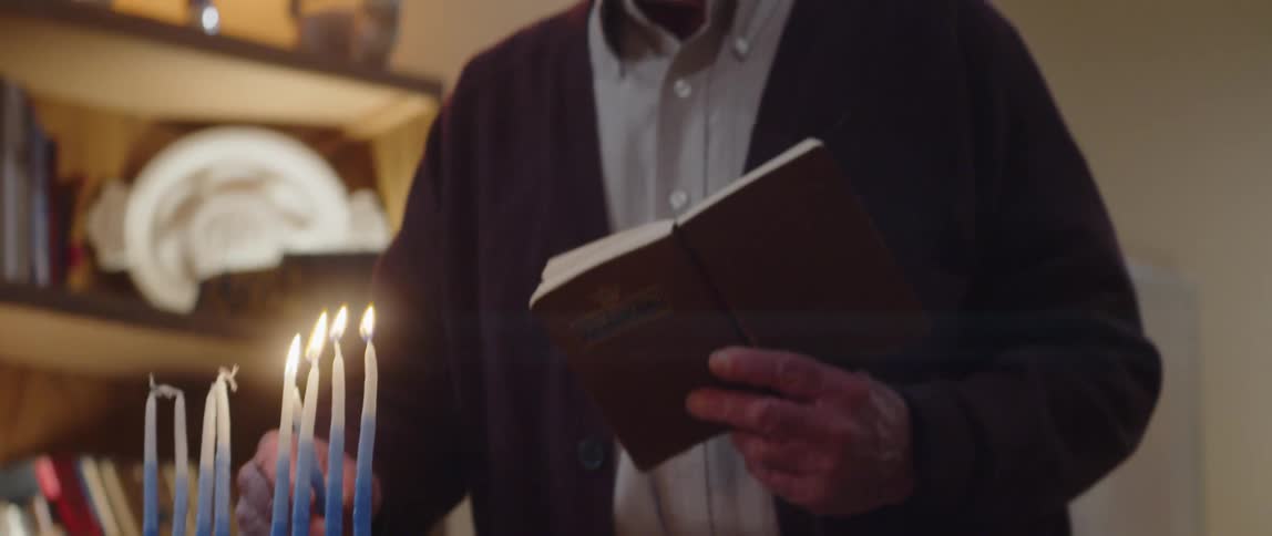 Jewish man praying in front of a menorah at home