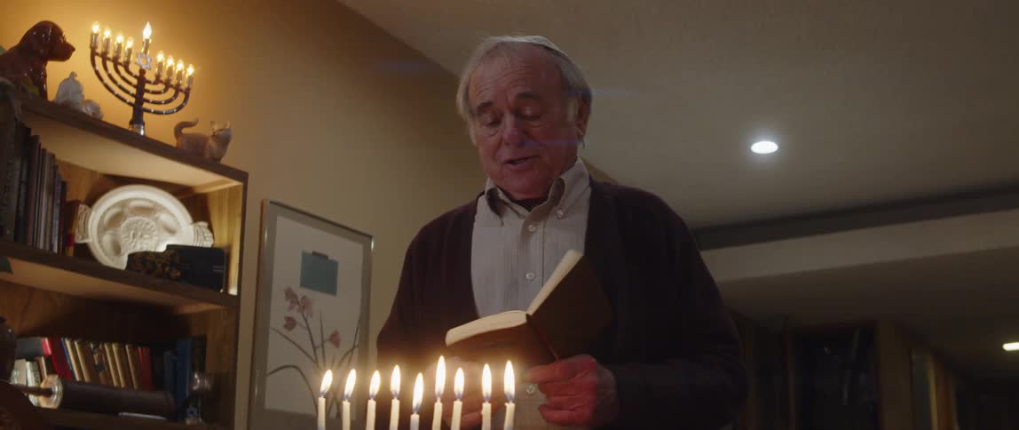Elderly man standing in a suit reading a bible in front of a cluster of candles