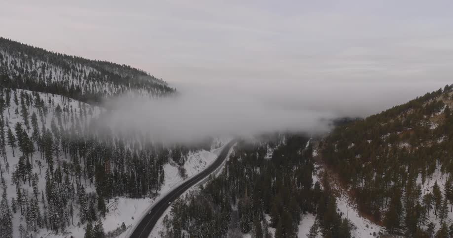 Aerial of a deserted road surrounded by forests and mountains during winter