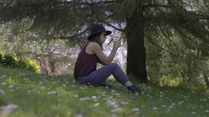 A young woman sits in a blooming field looking at her phone