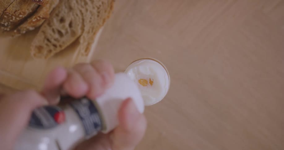 A person adds a pinch of cinnamon to a glass of eggnog