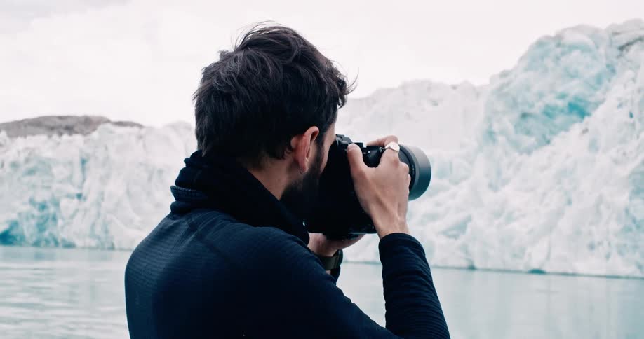 A photographer stands along the arctic coast taking pictures of icebergs