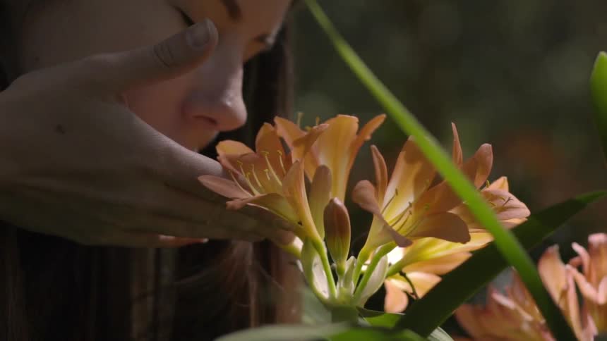 A woman bends down to smell a flower