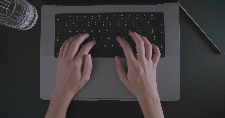 Closeup of a persons hands typing on a laptop keyboard