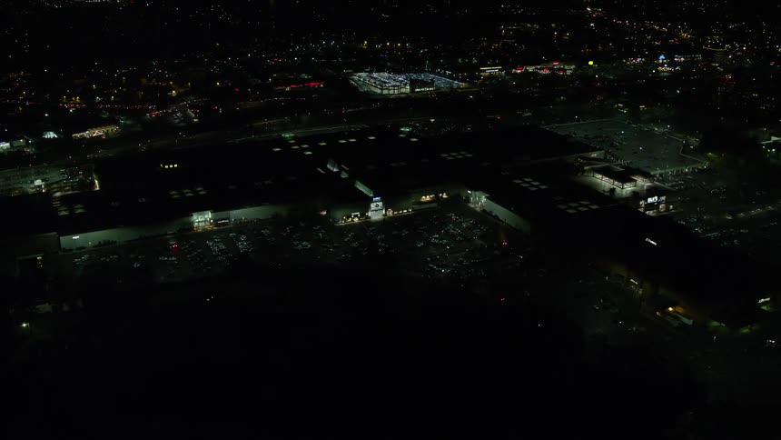 Highway traffic passes large building with a busy parking lot at night
